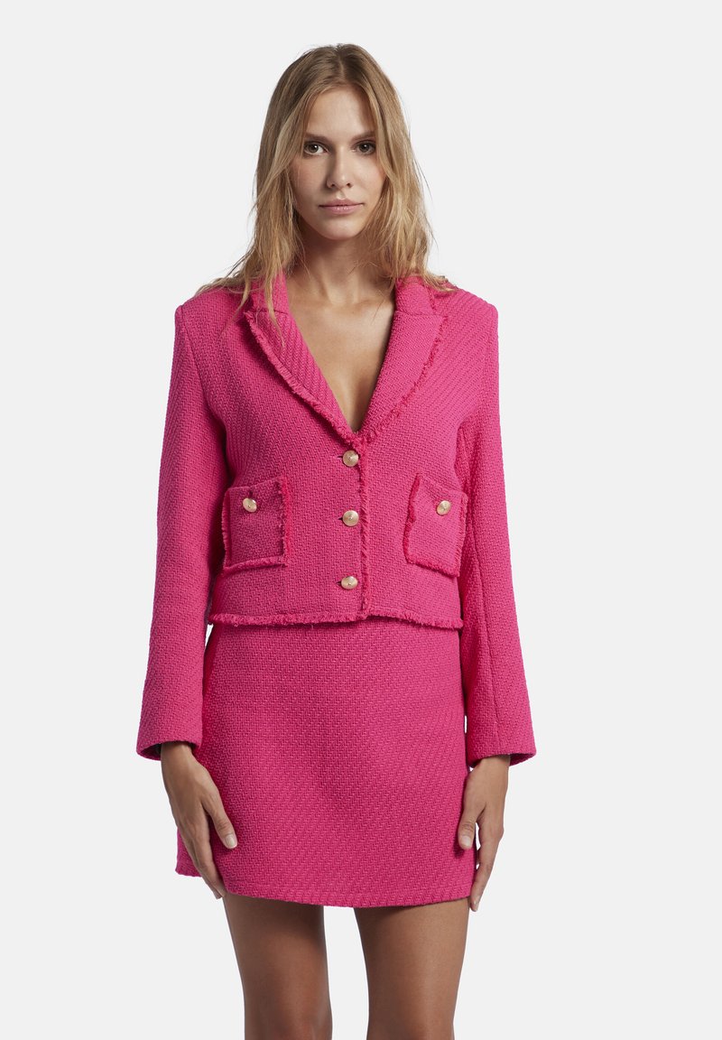 Roze cropped jack met rafelige randen, twee voorzakken en gouden knopen, gecombineerd met een bijpassende minirok in een gestructureerde stof.