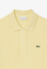 Polo giallo in un design slim fit, realizzato in tessuto testurizzato. Caratterizzato da un colletto con tre bottoni e un logo coccodrillo ricamato in verde.