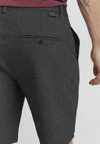 Gray shorts with a textured fabric, featuring a back pocket with a button closure and a small brand label near the waistband.