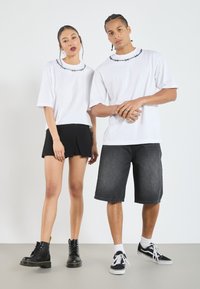 Hvite t-skjorter med svart piggtråddesign ved halsen, kombinert med et svart skjørt og mørk denimshorts. Brune svarte støvler og sneakers brukes.