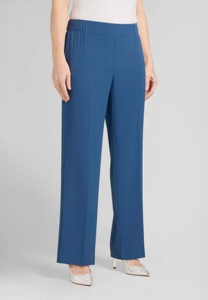 Pantaloni blu a gamba dritta con vita elastica indossati con scarpe bianche con tacco a punta e top bianco infilato.