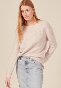 Maglione beige chiaro con motivo a spina di pesce, colletto rotondo e maniche lunghe, abbinato a una gonna in denim chiaro a vita alta.