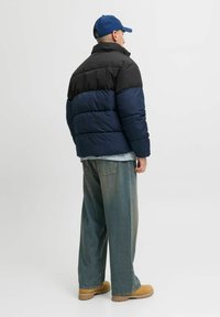 Czarna i granatowa kurtka puchowa o luźnym kroju, z wysokim kołnierzem. Noszona na jasnoniebieskiej, kraciastej koszuli i luźnych, jasnych dżinsach.