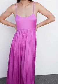 Robe maxi sans manches en tissu rose vif, avec un corsage ajusté et une jupe plissée. Comprend de fines bretelles et une texture douce.