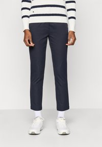 Tengerészeti slim-fit nadrág sima textúrával, elülső zsebbel, fehér sportcipővel és bordázott kötött csíkos pulóverrel párosítva.