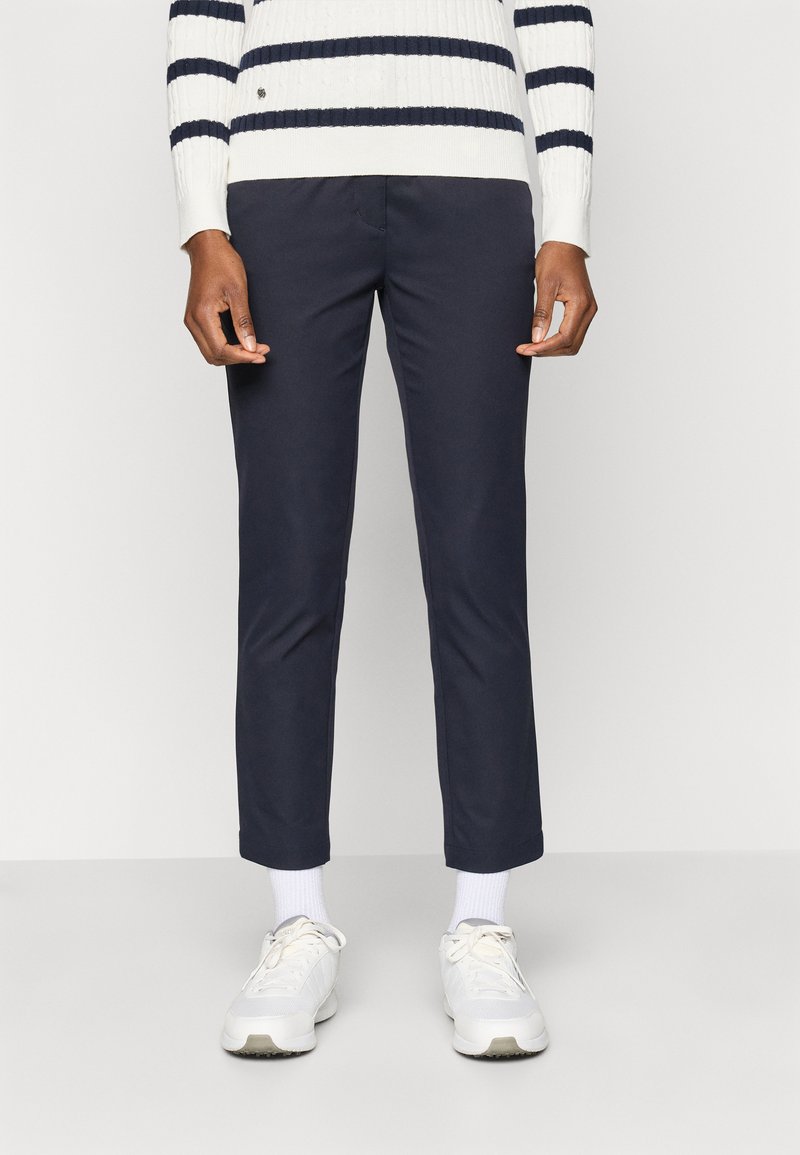 Tengerészeti slim-fit nadrág sima textúrával, elülső zsebbel, fehér sportcipővel és bordázott kötött csíkos pulóverrel párosítva.