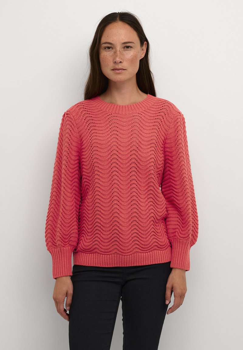 Lightweight coral knit sweater with a wave pattern, ribbed neckline and cuffs, and structured balloon sleeves. Paired with black pants.