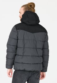 Puffjakke i mørkegrå med sort hætte, der har et chevron-design og vandret syninger. Materialet ser blødt og isoleret ud.