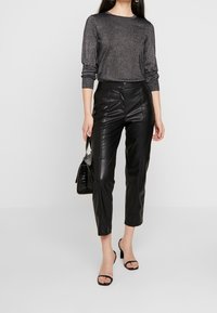 Svarta lädercroppade byxor i kombination med en glittrig svart långärmad topp. Tillbehör inkluderar en liten svart handväska och svarta klacksandaler.