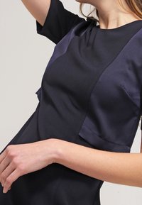 Abito della marina con maniche corte, caratterizzato da un design a blocchi di colore in tonalità scure. Texture liscia con dettagli di cucitura sottili e silhouette aderente.