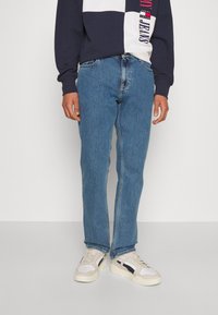 Blå denimjeans med rak passform, med en klassisk femfickdesign och subtila blekningar. I hop med beige sneakers.