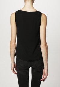 Haut noir sans manches en tissu léger, avec un col arrondi et une coupe décontractée, avec un ourlet arrière légèrement plus long.