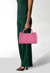 Borsa in pelle rosa con una texture liscia, forma strutturata e doppi manici. Abbinata a un abbigliamento verde e scarpe con tacco nere.