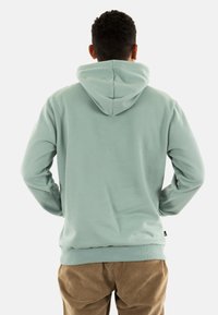 Felpa con cappuccio in morbido tessuto verde menta. Presenta una vestibilità rilassata con polsini e orlo a coste, e un'etichetta sul lato.