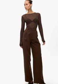 Haut en maille marron à manches longues avec des embellissements dispersés, associé à un pantalon marron taille haute. Détail notable de boutons à la taille.
