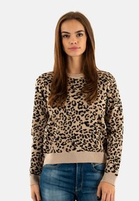 Suéter de estampado de leopardo en beige y negro. Textura de punto con cuello y puños acanalados. Combinado con jeans de mezclilla azul.