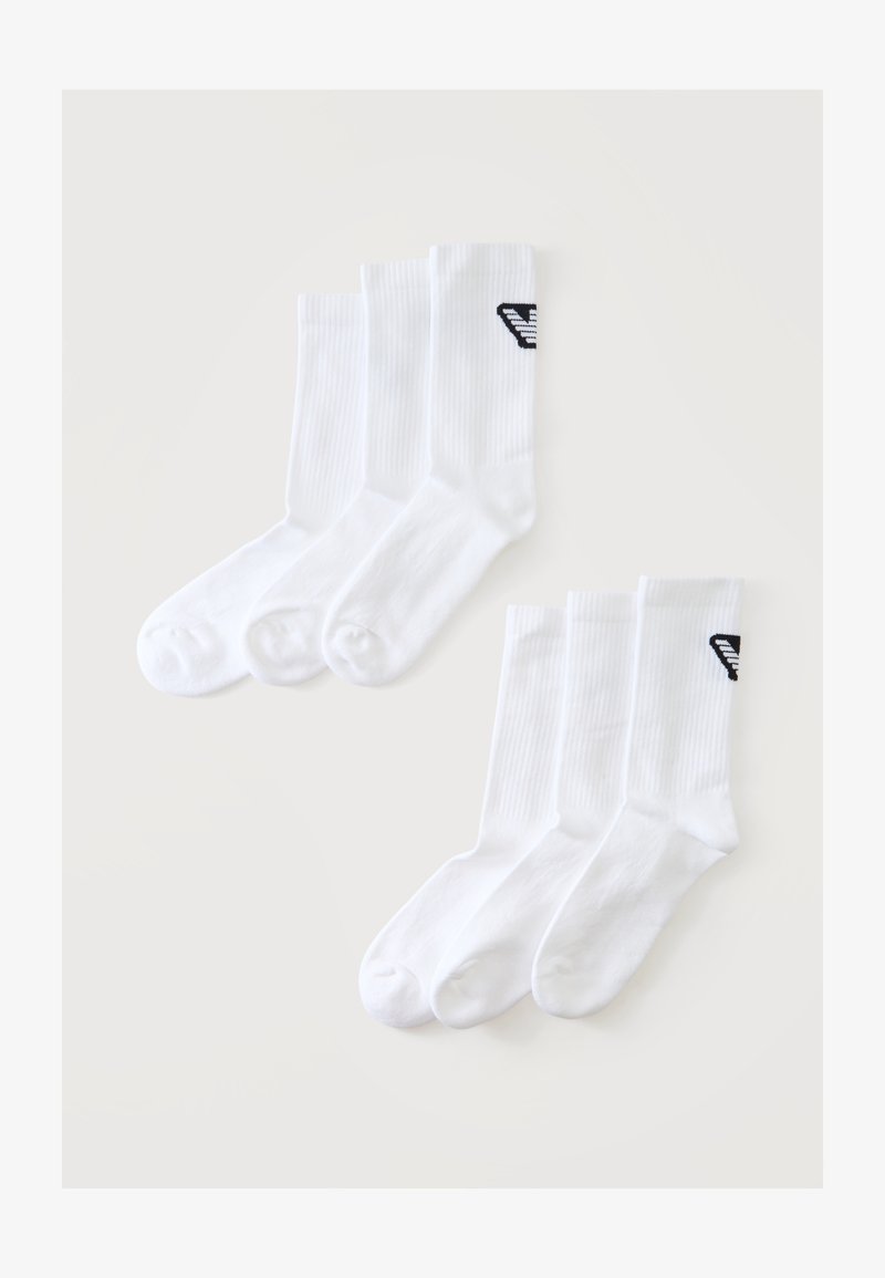 Deux ensembles de trois chaussettes blanches à logo noir sur le dessus, présentées à plat sur un fond clair.