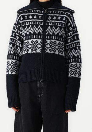 Navy and light gray knitted zip-up sweater with geometric patterns, ribbed hem and cuffs, relaxed fit, and high collar detail.