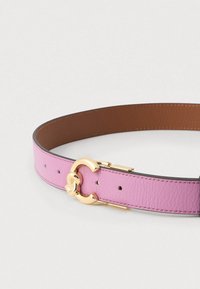 Rožinė odinė diržas su auksinio atspalvio sagtimi, kurios dekoratyvinis dizainas primena S raidę. Vidaus dalis pagaminta iš lygaus rudo odos.