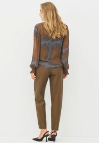 Prosojna rjava bluza z sivo geometrijsko vzorcem, dolgi napihnjeni rokavi, združena z rjavimi hlačami ravnega kroja in črnimi petami.