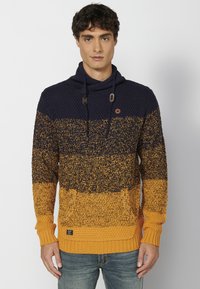 Sudadera de punto en navy y mostaza con un patrón degradado, que cuenta con un cuello de capa, cordones y un bolsillo frontal. Tela texturizada.