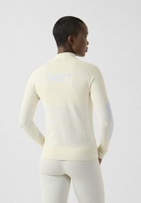 Top sportivo a maniche lunghe di colore giallo chiaro con righe testurizzate, collo alto e logo sul retro, abbinato a leggings coordinati.