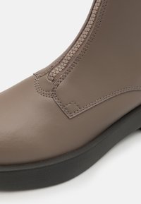 Brune lær ankle boot med en teksturert overflate, glidelås på siden og kontrastsøm. Har en svart gummisåle.