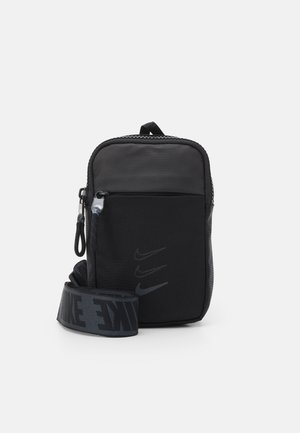 Mała czarna torebka na ramię z przednią kieszenią zapinaną na zamek, regulowanym paskiem z napisem "NIKE" oraz trzema logo Swoosh na przednim panelu.