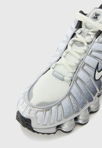 Nike sneaker featuring a white mesh upper, gradient grey accents, a prominent rounded sole, and gray laces with a silver swoosh logo.