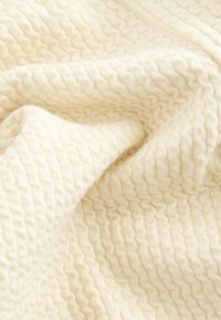 Tessuto di crema testurizzato con un sottile motivo ondulato, che mostra un aspetto morbido e tessuto. Il materiale è leggero e soffice.