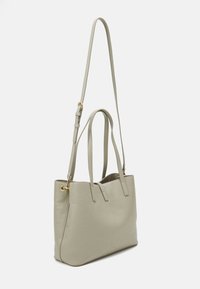 Ljusgrön tygväska i texturerat syntetmaterial med präglad logotyp, två axelremmar och en avtagbar justerbar rem.