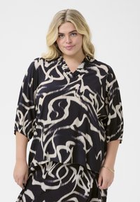 Top astratto nero e crema con scollatura a V e maniche a tre quarti, realizzato in un tessuto leggero e liscio.