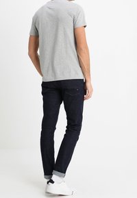 T-shirt en coton gris à col rond, associé à un jean slim en denim foncé, avec les manches retroussées et des baskets blanches. Design minimaliste.