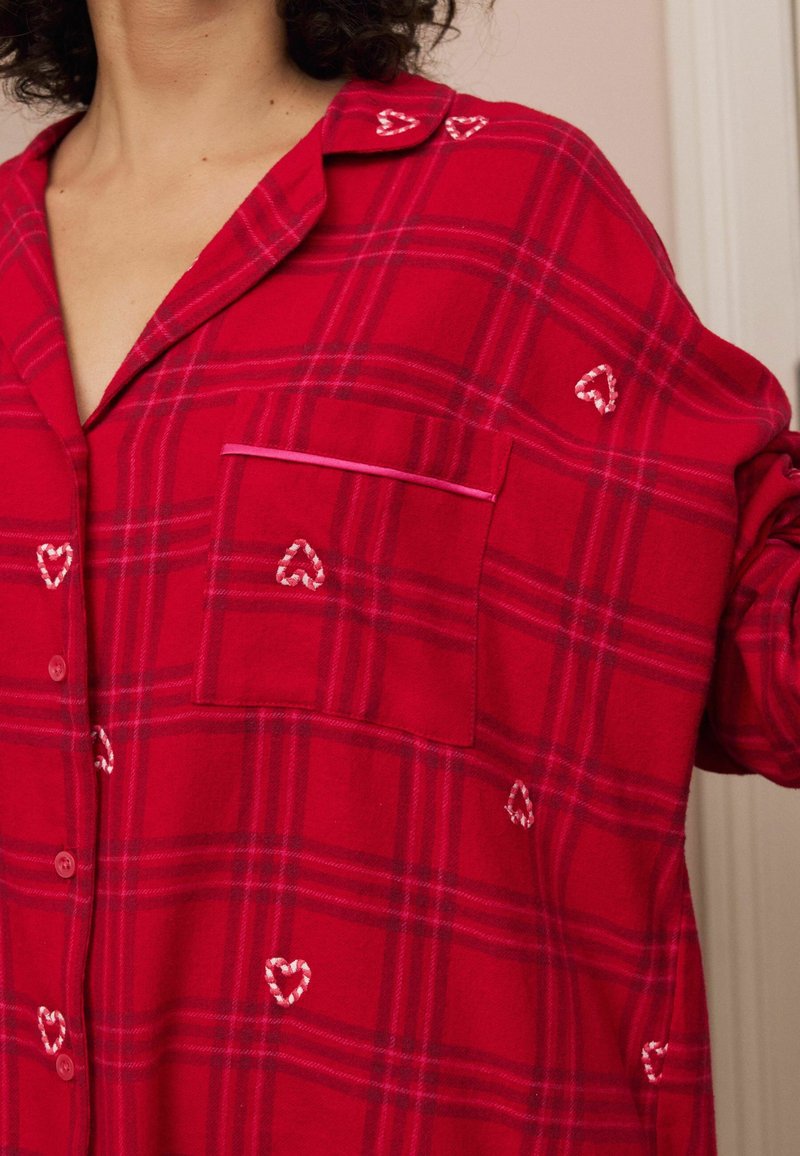 Raudona languota flanelinė marškinė, turinti kišenę, širdelės siuvinėjimą ir kontrastingą apdailą. Marškiniai su mygtukais, relaxed fit ir minkšta tekstūra.