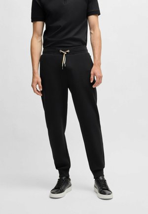 Pantalons de jogging noirs avec une taille à cordon, design fuselé et ourlets côtelés. Assortis à des baskets noires. Texture de tissu lisse.