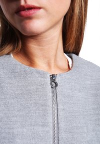 Giacca in pile grigia con zip silver, colletto alto e texture liscia. Il tessuto appare morbido e leggero.