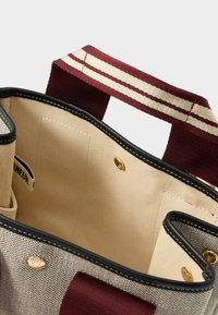 Καμβάς τσάντα ώμου με μπεζ εσωτερικό, χειρολαβή σε μπορντό και λευκές ρίγες, μαύρη επένδυση και χρυσά κλείσιμο με κουμπί.