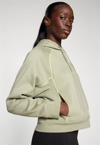 Hoodie verde claro com detalhes amarelos, apresentando um bolso canguru, capuz com cordão e punhos canelados. Tecido macio e texturizado.