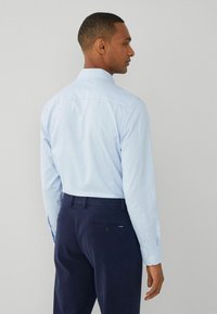 Camicia a scacchi blu chiaro con maniche lunghe, polsini con bottone e un yoke posteriore, abbinata a pantaloni blu navy con tasca posteriore.
