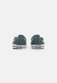 Zaļi kanvas zema augstuma sporta apavi ar baltām gumijas zoleēm, pieticīgām šuvēm un "Converse All Star" zīmolu uz papēža.