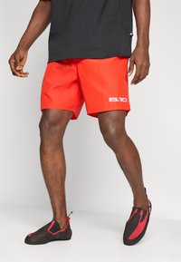 Κόκκινα μαγιό σορτς με ομαλή υφή και λευκό λογότυπο "5.10". Συνδυασμένα με μαύρα παπούτσια αναρρίχησης που διαθέτουν κόκκινες λεπτομέρειες και εφαρμοστή εφαρμογή.