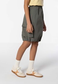 Gonna khaki con cintura elastica e tasche laterali, abbinata a sneakers bianche con dettagli arancioni e calze a coste.