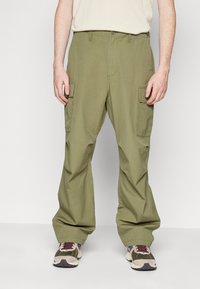 Olive green cargo pants with a loose fit, featuring multiple side pockets and a zippered fly. Pairing with multicolored athletic shoes.