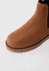 Bottine Chelsea en cuir marron avec semelle cousue, bout arrondi et panneau latéral élastique sur fond blanc.