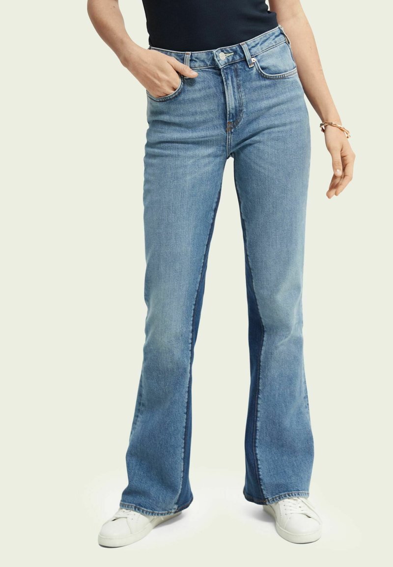 Ljust blå jeans i bootcut-modell med hög midja, som har framfickor, dragkedja och något ljusare blekta paneler längs sidorna.