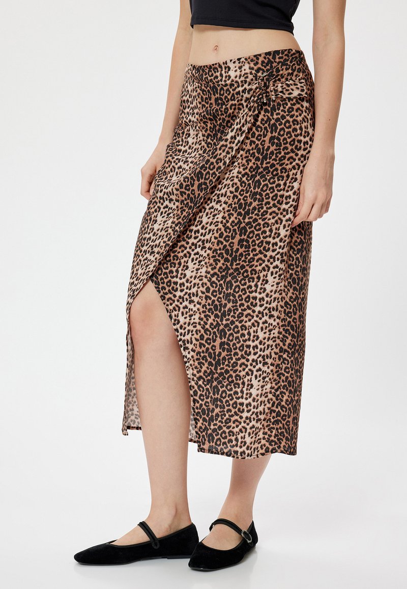 Leren midi-rok met luipaardprint en een zijsplit, gemaakt van lichte stof. Kenmerkt zich door een geknoopt detail bij de taille, gecombineerd met zwarte platte schoenen.