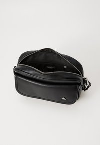 Borsa nera in pelle con finitura testurizzata, dotata di chiusura con zip, tasca interna e un accent metallico triangolare. Vista aperta.