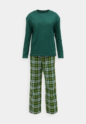 Maglione a maniche lunghe verde scuro abbinato a pantaloni a gamba larga a quadri verde, bianco e giallo su sfondo bianco semplice.