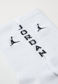 Par de calcetines blancos acanalados con logotipos de Jumpman en negro y texto "JORDAN" tejido cerca del puño superior.