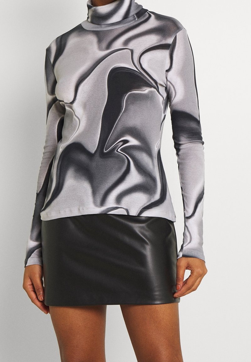 Langärmliges Turtleneck-Oberteil in Grau mit schwarzem abstraktem Marmor-Muster, kombiniert mit einem kurzen, schwarzen Kunstleder-Rock. Glatte Textur überall.